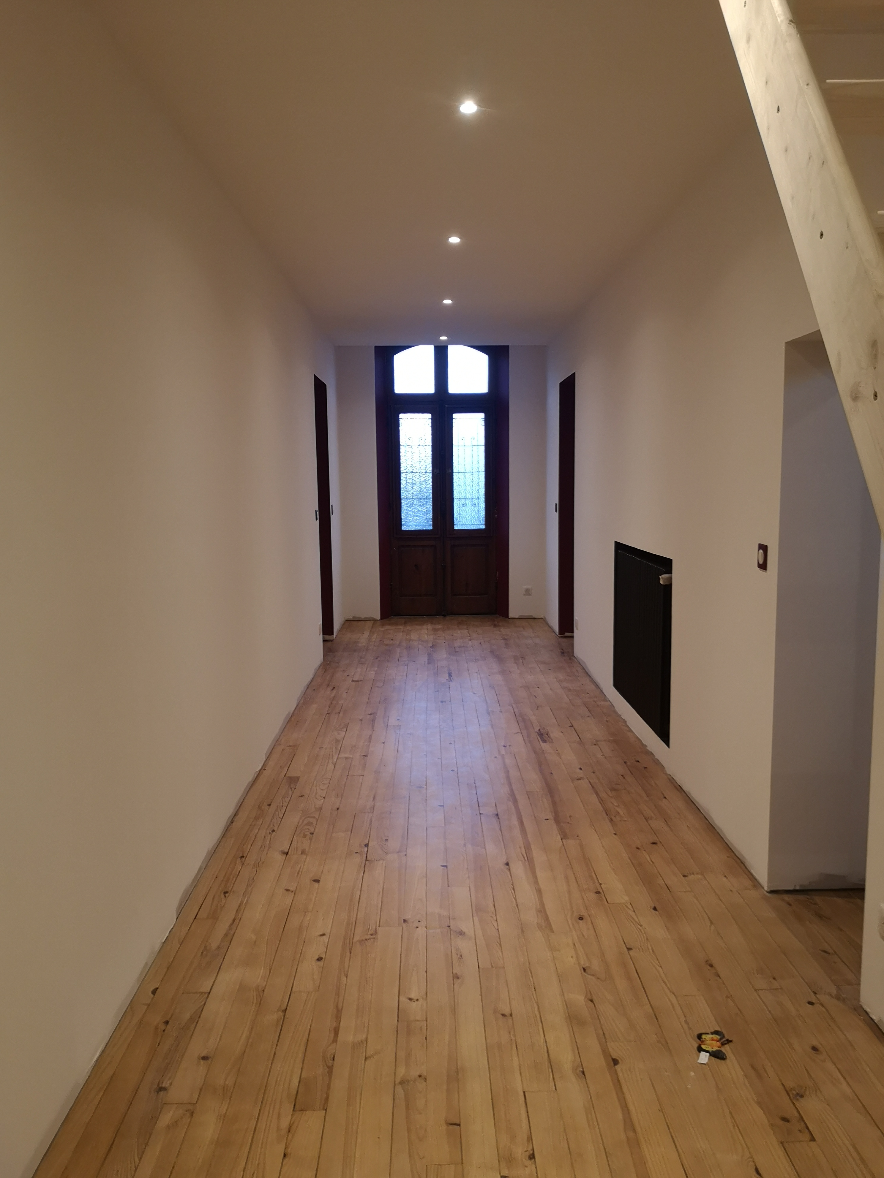Couloir rénové avec murs blancs, parquet bois, éclairage et radiateur noir