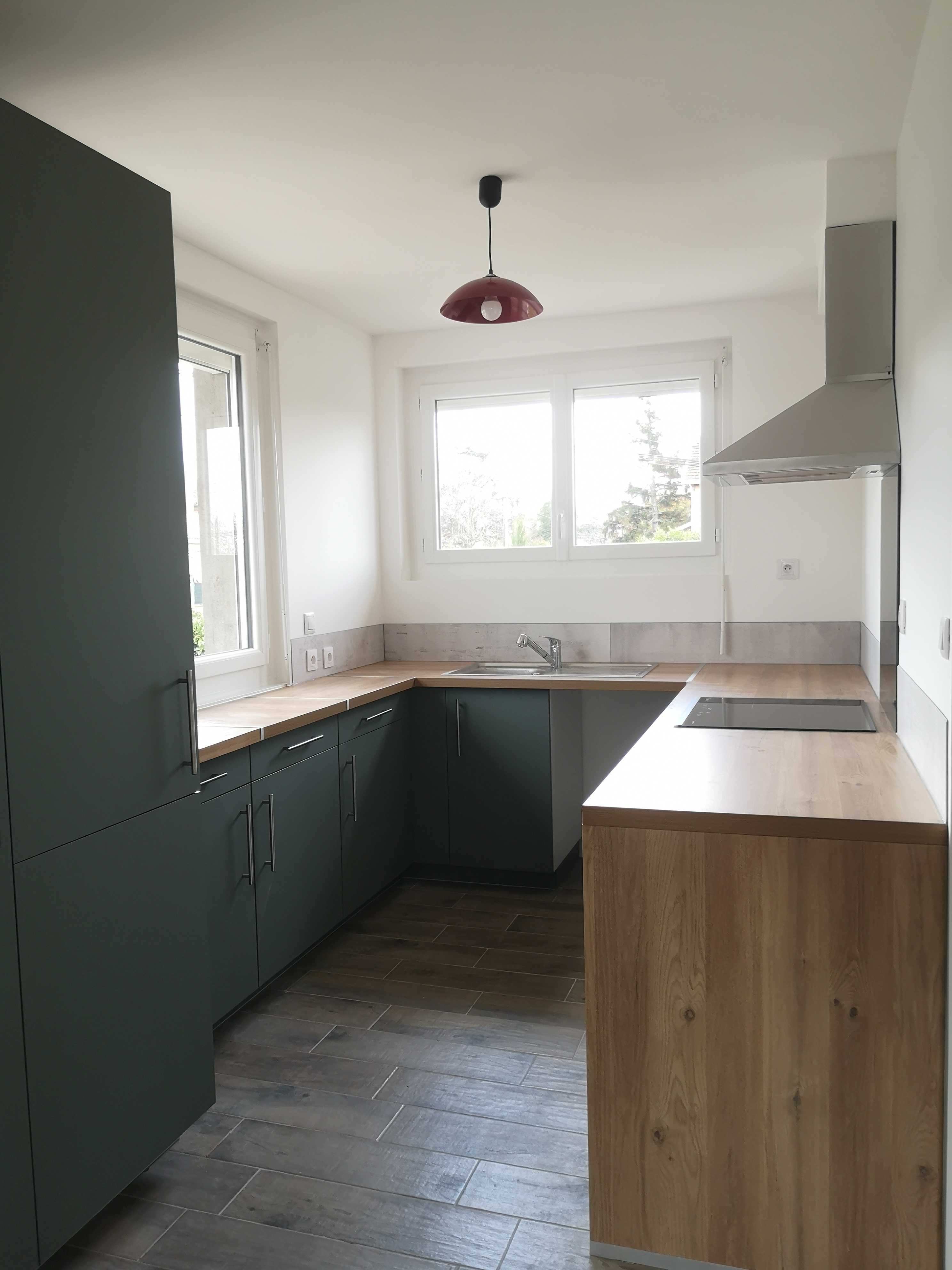 Cuisine équipée avec façades vert foncé, plan de travail bois et sol imitation parquet